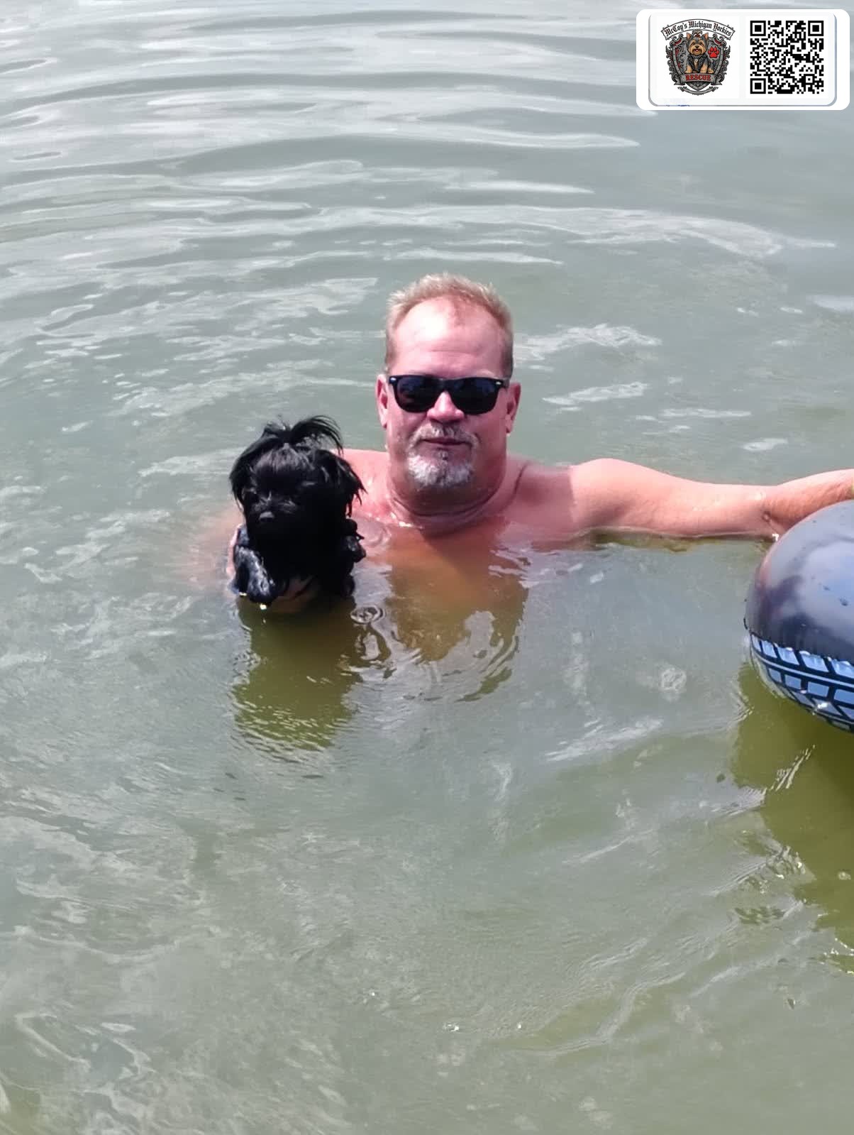 Eric swimming in the lake while holding a small black Yorkshire Terrier safely beside him
