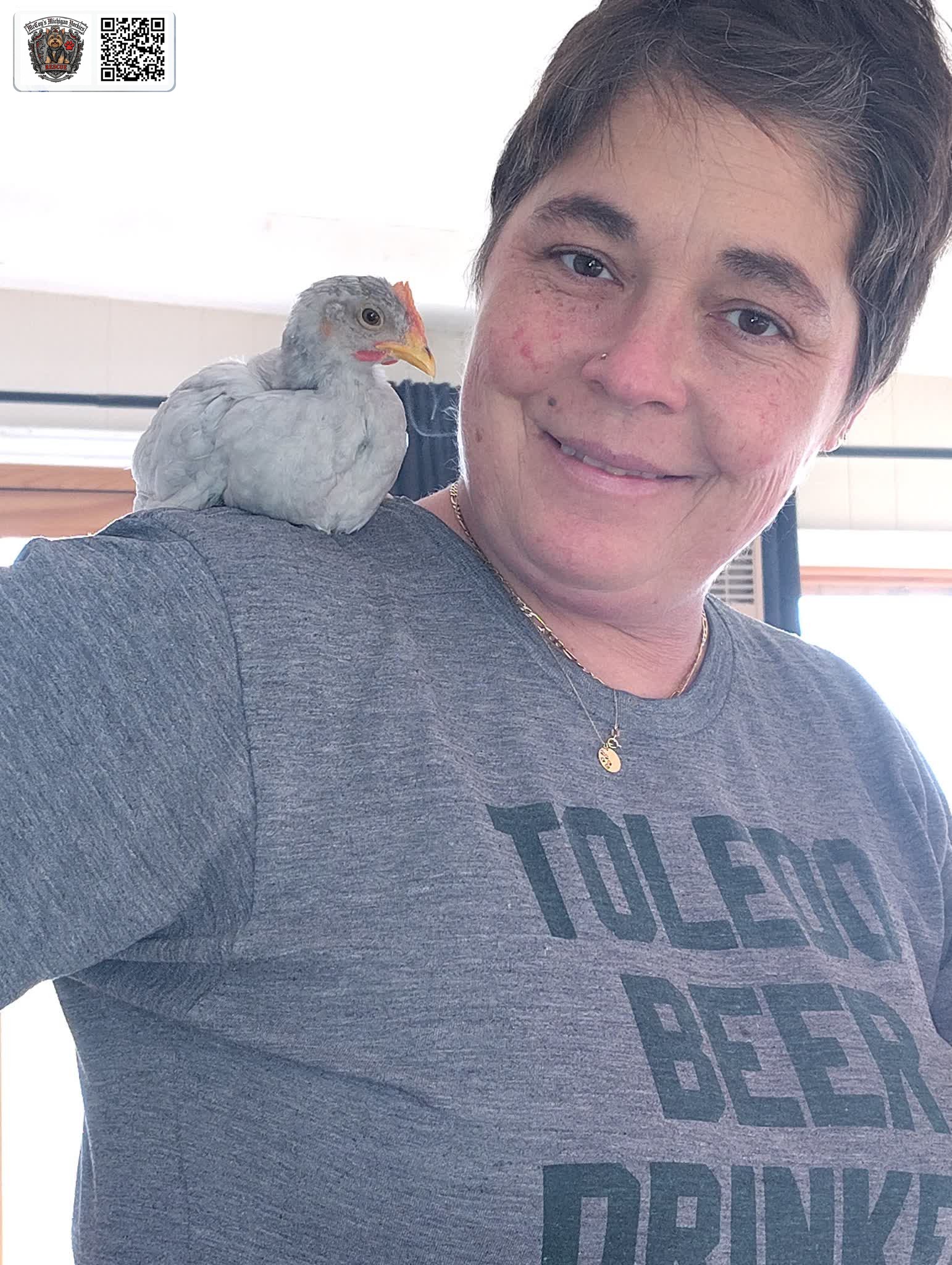 Crystal smiling with a young white chicken perched on her shoulder